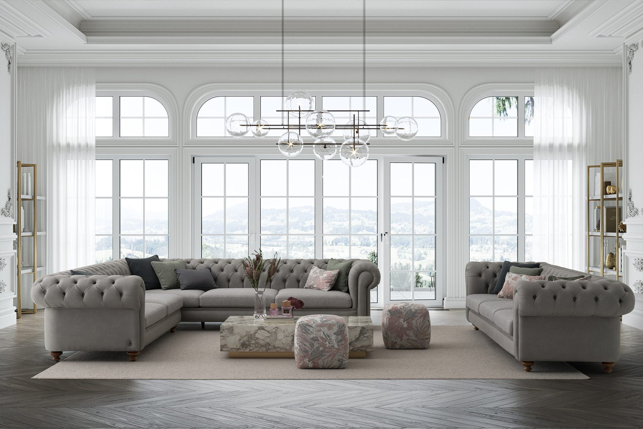 A luxurious living room with gray tufted sofas, arched windows with white drapes, a chandelier, and decorative ottomans.