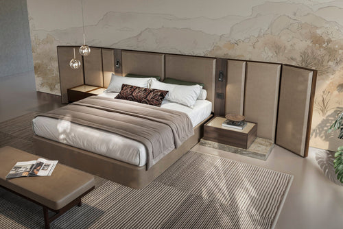 Modern bedroom with tall upholstered headboard, matching nightstands, low platform bed, and a bench at the foot of the bed against a textured stone-effect wall.